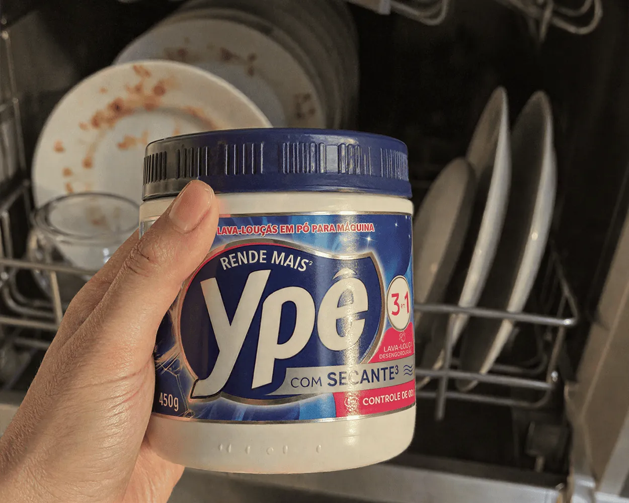 pessoa segurando o produto sabão de lava louças ype 450g e uma lava louças aberta ao fundo